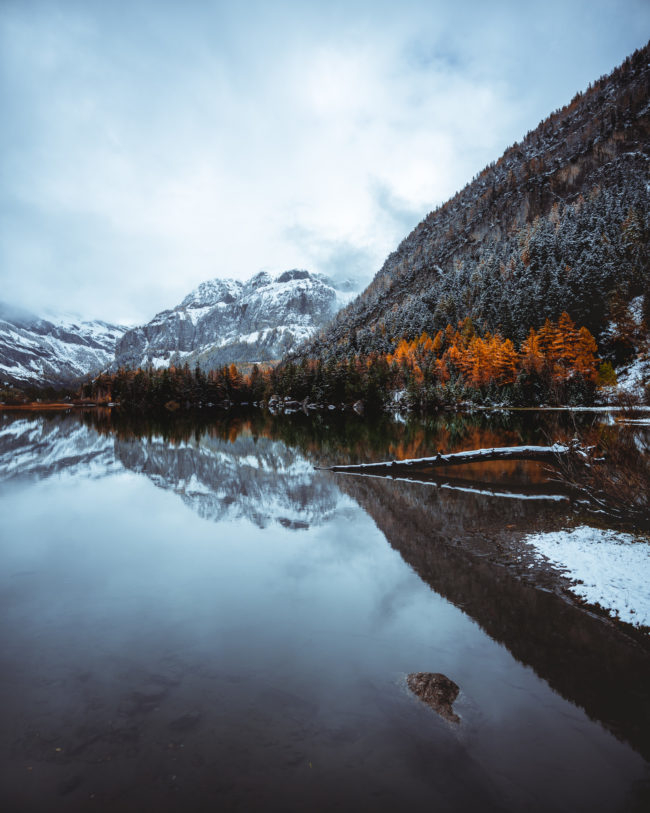 the lake of derborence is calm with a perfect reflection of the mountain and the trees